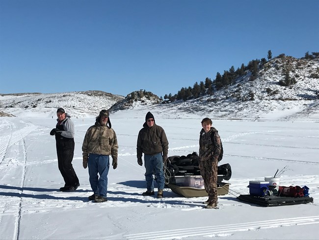 Four men carry ice fishing gear on sleds across a frozen lake