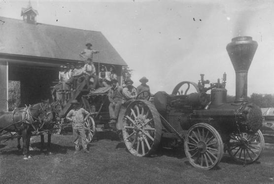 Black and white photo of a steam engine and crew posing in front of an old building.