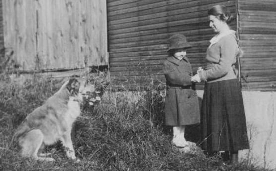 Historical photo of Mother and child on the farm with their dog and barn
