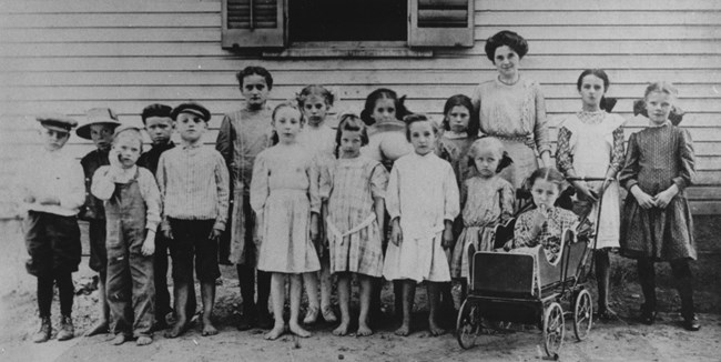 Black and white photo of a teacher and fifteen students standing outside a building.