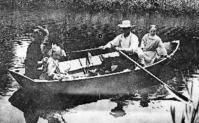 Black and white photo of a family in boat in Everett. A man is rowing the boat, a little girl sits behind him, a woman sits across from them with another little girl next to her.