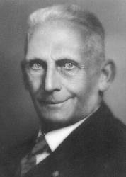 Black and white portrait of an elderly man with gray hear wearing a white shirt, tie and dark jacket.