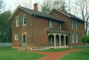 A two story brick home with a covered porch on a grassy yard with a path leading up to the house.