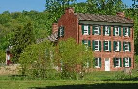 Green trees surround a three-story red brick building with rows of white windows with green shutters.