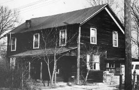 Black and white photo of Everett dance hall, now Everett Ranger Station. A dark colored two-story house with an awning over the front door, and windows on the first and second floor.
