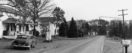 Black and white photo of Everett Road small businesses. A rural road with quaint structures on the left side of the road. Trees are in the background.