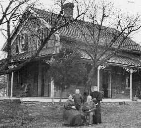 Historic photo taken of a family of four posing in from of their farmhouse.