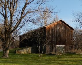 Exterior of a brown wood-sided barn; an earthen ramp leads up the left side; grass and leafless trees surround the barn.