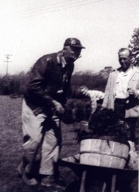 Grainy black and white photo of three people outside, loading a wheelbarrow.