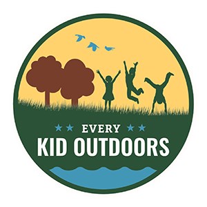 A round illustrated logo: yellow sky, brown trees, blue birds, and green children playing in green grass; white text reads: Every Kid Outdoors.