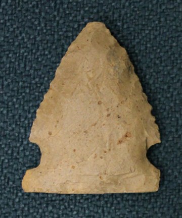 A beige triangular arrowhead with knapped edges, on a blue background.