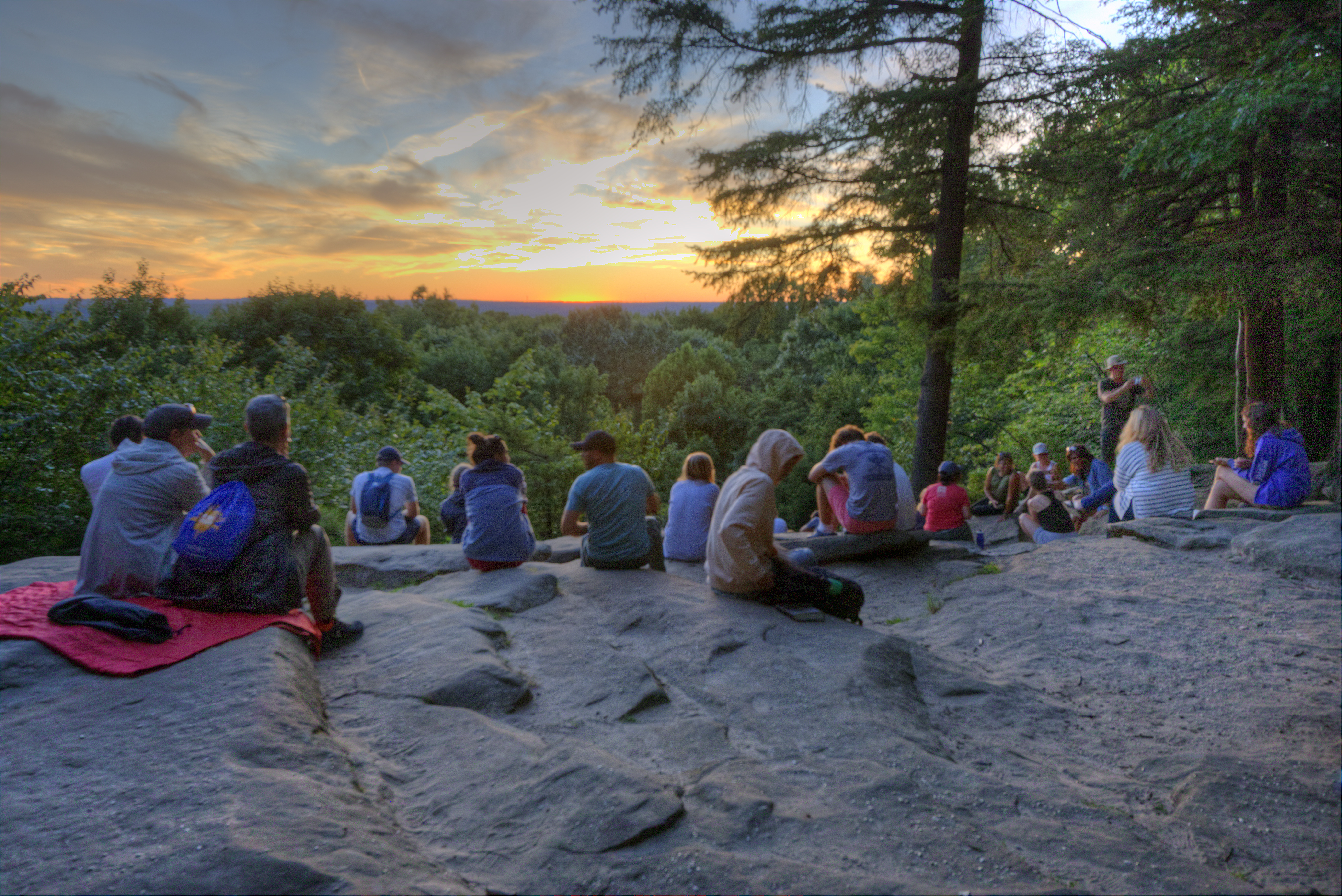People Enjoying the Ledges Overlook at Sunset People sitting on a rock ledge at sunset overlooking a green forest