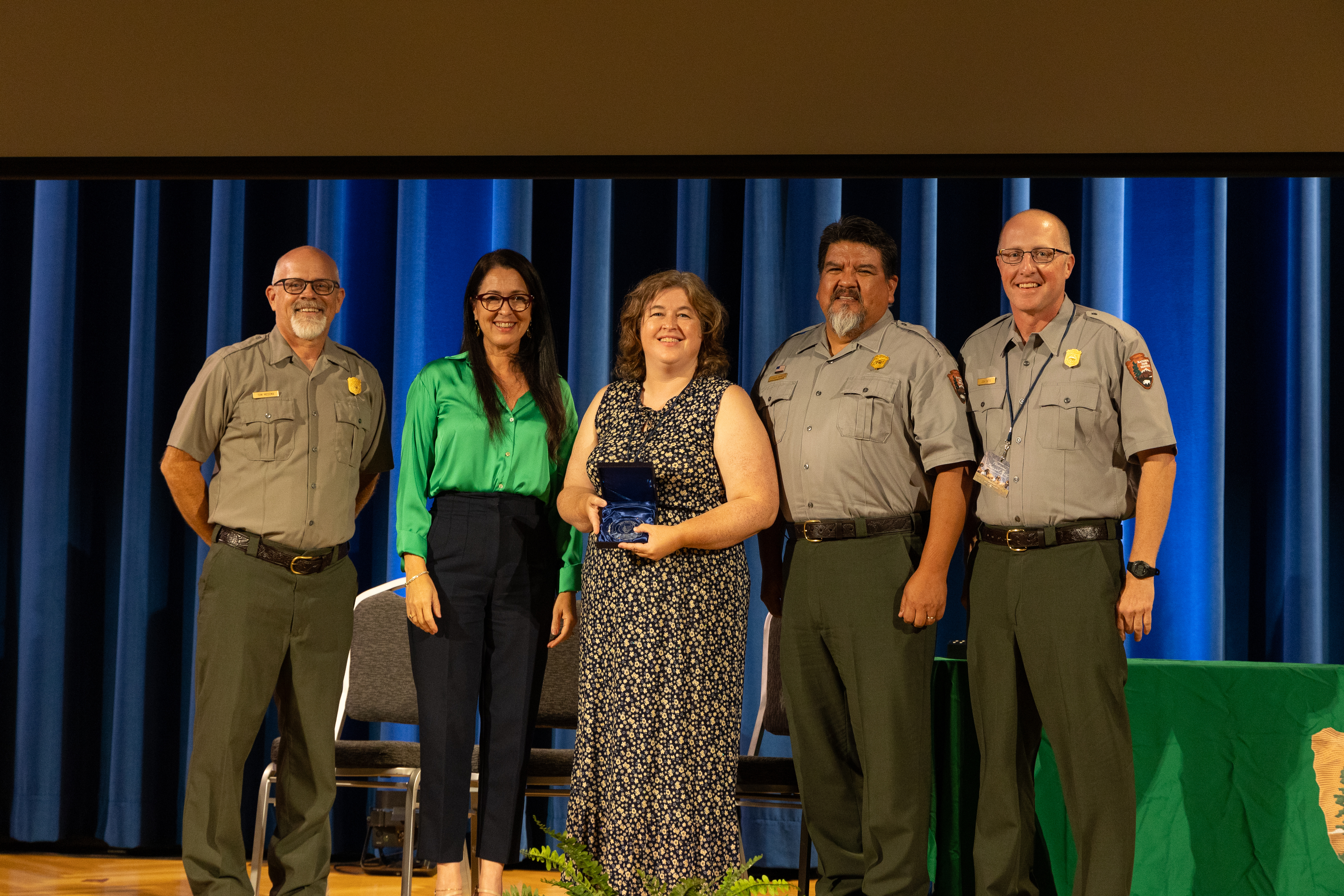 Candance and Josh Bates Accept the Hartzog Award Three rangers stand with two people on a stage holding and award.