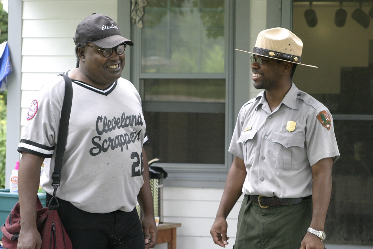 Two African American men smile at each other. One wears a baseball shirt and cap. The other wears a ranger uniform.