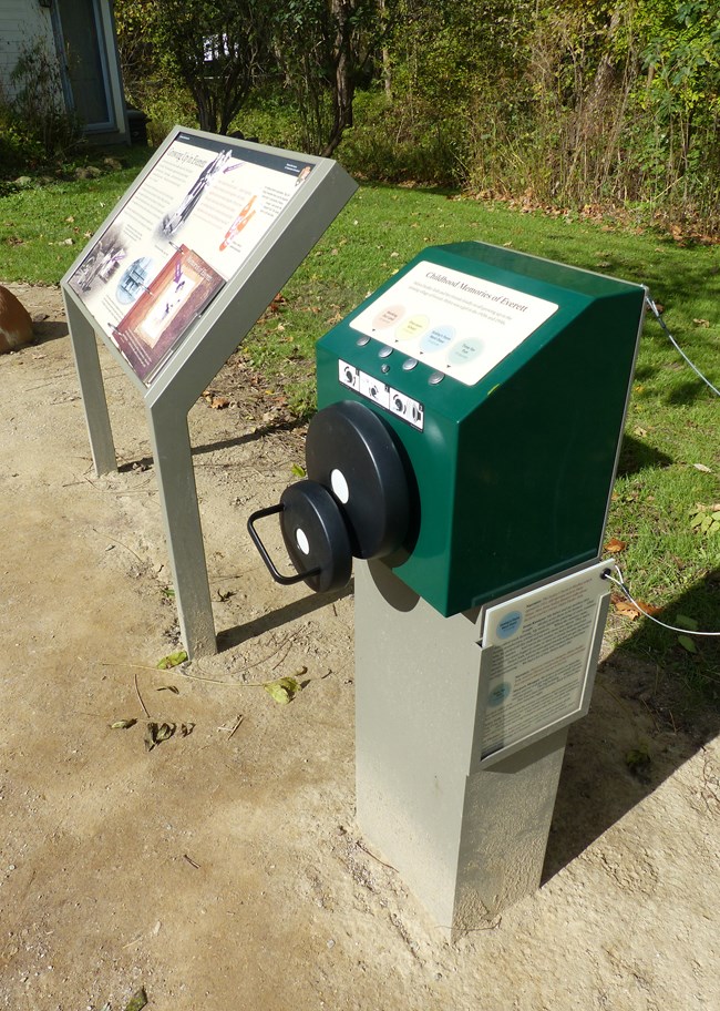 A green box with four message buttons, a hand crank, and a tethered script stands beside a panel with a flipbook.