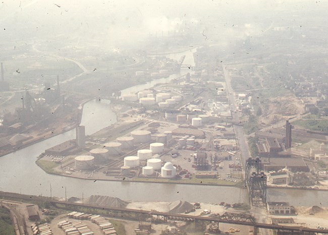Aerial Views Cuy Riv in Cleve June 1974 A hazy view of industry along the river: large white cylindrical tanks, railroad bridges and smokestacks dominate the landscape.
