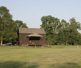 Exterior of a two-story brown barn surrounded by a grassy field and trees in the background.