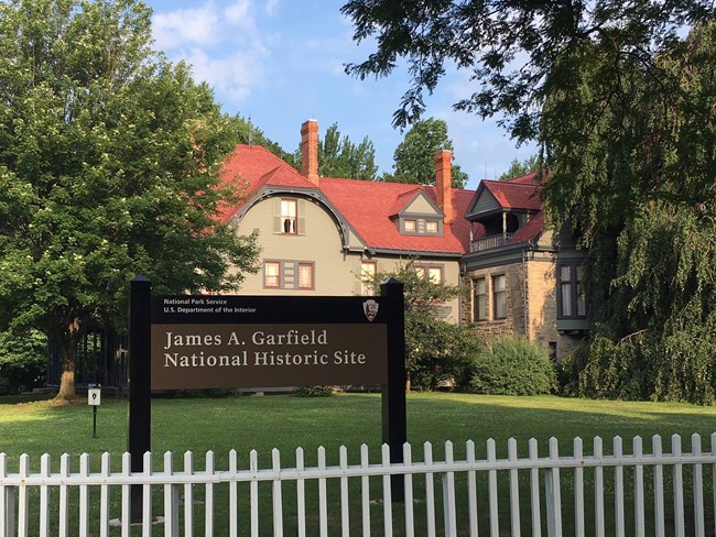 Exterior of a three-story building with a red roof; a sign in front reads James A. Garfield National Historic Site.