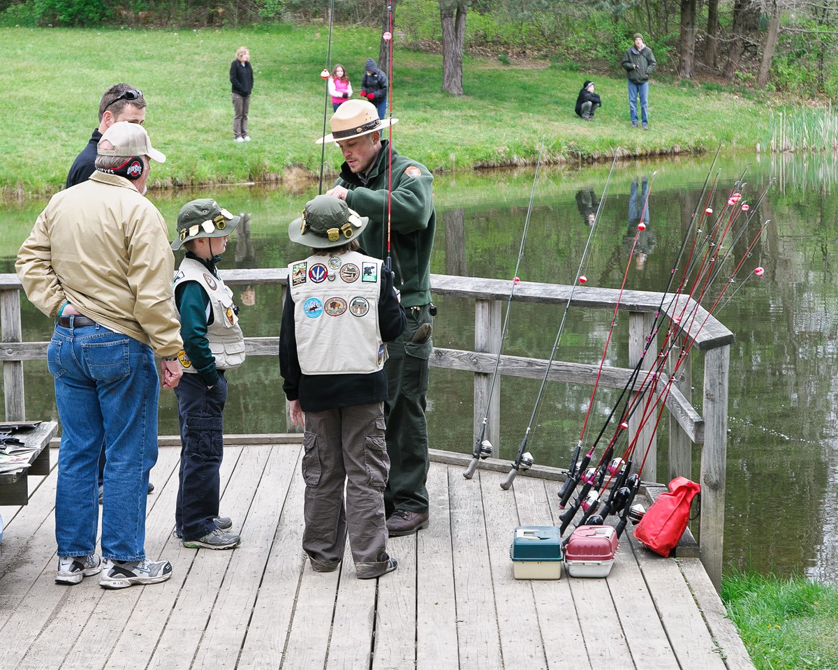 ranger helping two boy scouts take a fish off of a line ranger helping two boy scouts take a fish off of a line