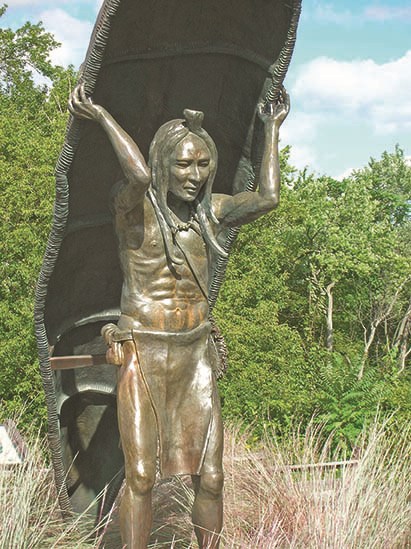 Bronze statue of an American Indian holding a canoe over his head.