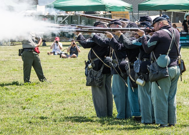 Union soldiers fire their rifles during a living history demonstration.