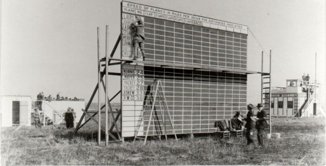 Air Race Scoreboard Black and white image of The official scoreboard with scorer updating with racers for Event No. 2, the National Cash Register Trophy race.