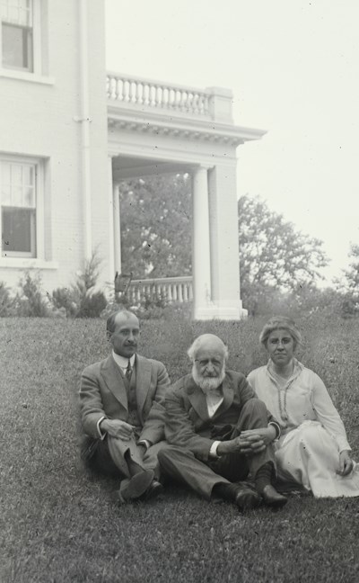 Three people sitting on a hill in front of a large house