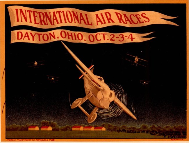 Air Races Ad Poster Colored advertisement with the words "International Air Races Dayton, Ohio. October 2-3-4". Cartoonized airplanes appear in the center of the ad. Small houses with red roofs appear along the bottom of the image.