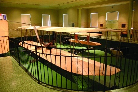 The 1905 Wright Flyer III in a sub-level pit surrounded by steel fencing.