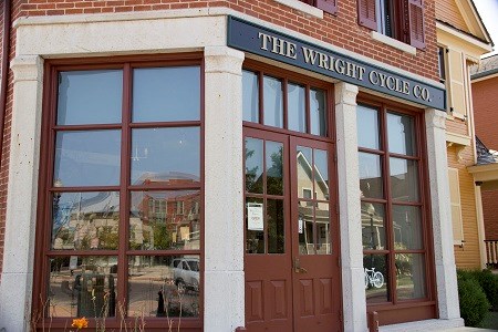 A building store front with several panels of glass displays and a double-entry door in the center and a shop sign above it all.