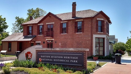 A long, two-story brick building and a stone sign in the front with name of the park on it.