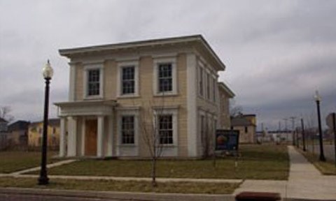 A yellow and white two-story home sits at the intersection of S. Williams and West Fourth. The wood finished front entrance is flanked by white columns on the far left as windows, trimmed in white, consume the remaining facade.