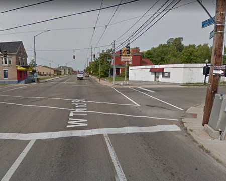 A city intersection with street lights hanging above and white stopbars and crosswalks on the pavement