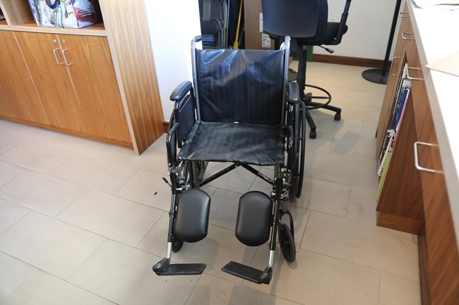 An empty, black, manual wheelchair is positioned behind the front desk in the visitor center.