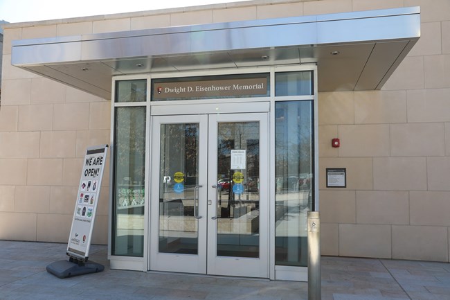 Double glass doors allow visitors to enter the visitor center/bookstore. A wheelchair-accessible button is positioned to the right of the entrance on a separate column.