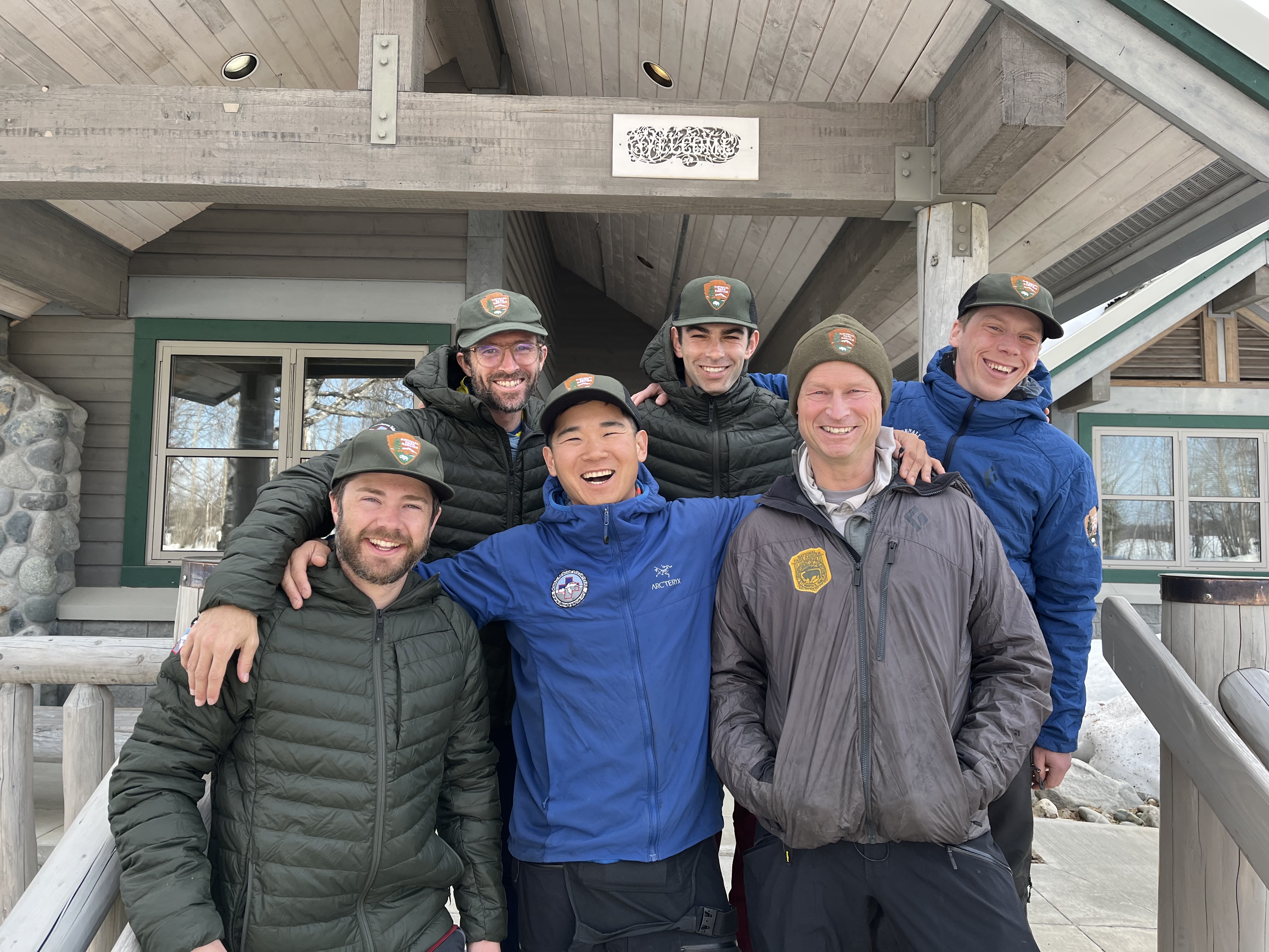 Denali 14K Patrol #1 Six smiling men in winter clothing stand on steps outside a ranger station