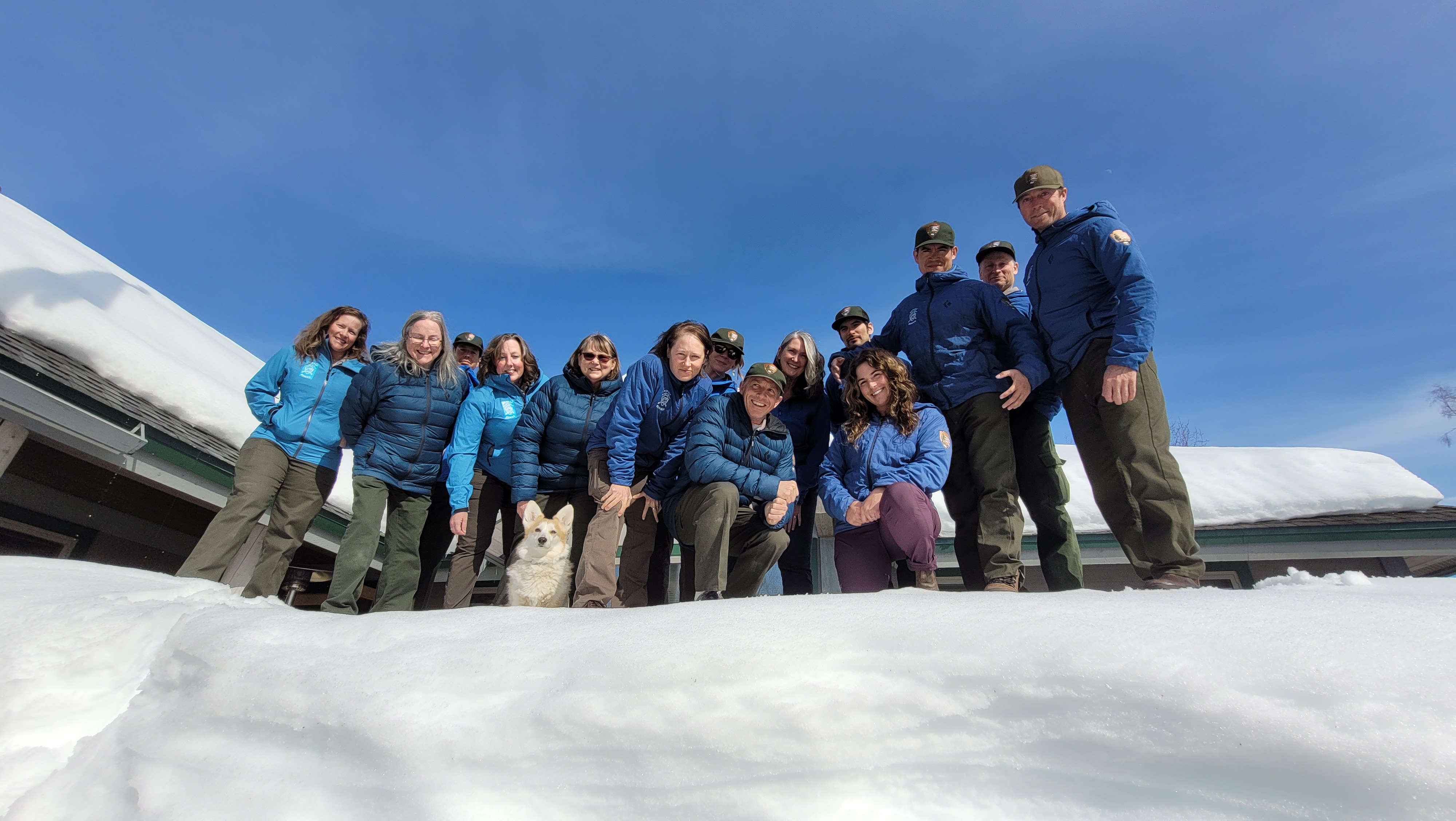 2022 Talkeetna Ranger Station Staff Photo A work team looks down at the camera from a high snow bank outside of a ranger station