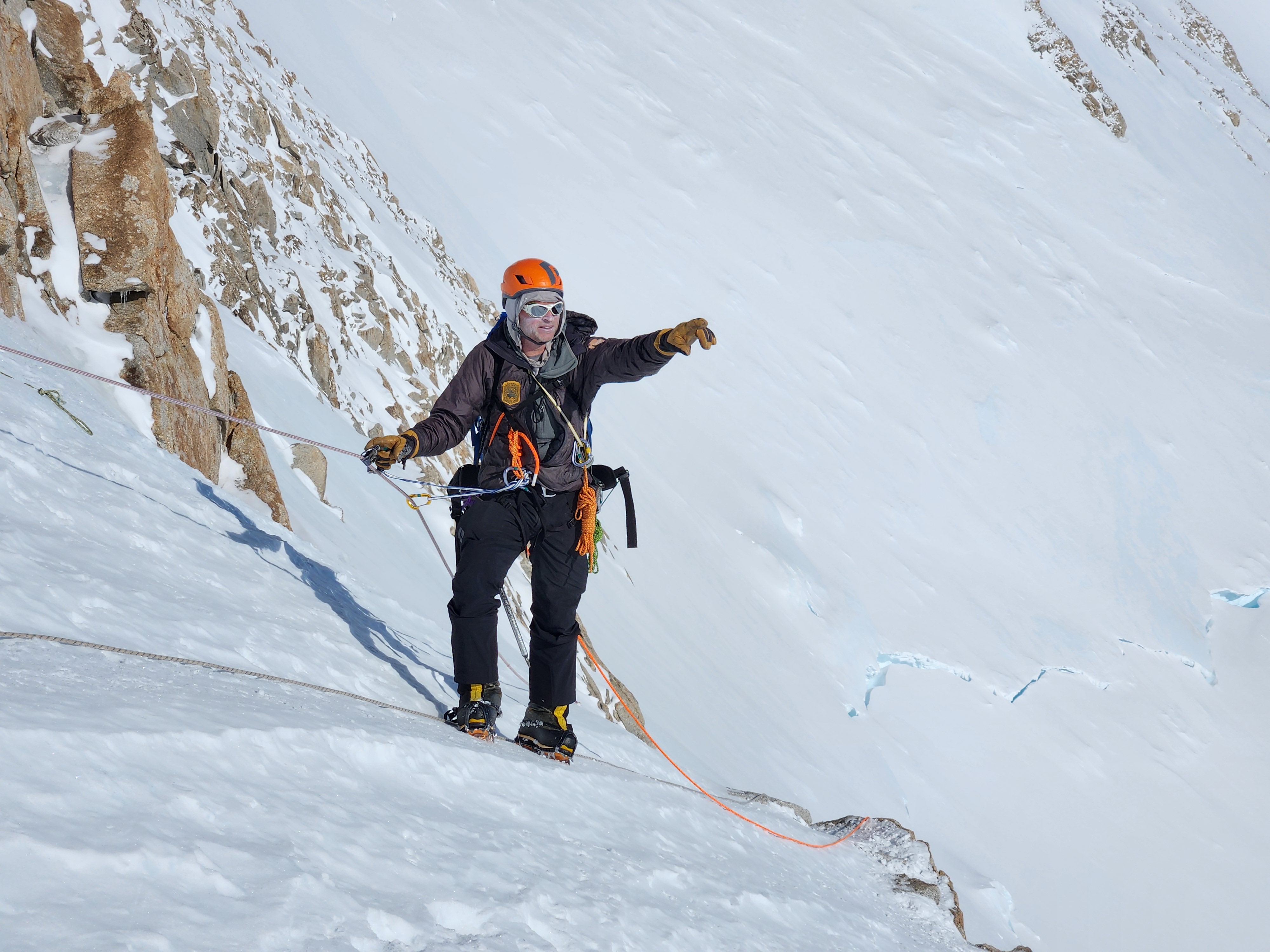 A ranger points in the distance while climbing a steep snow slope on a rope line