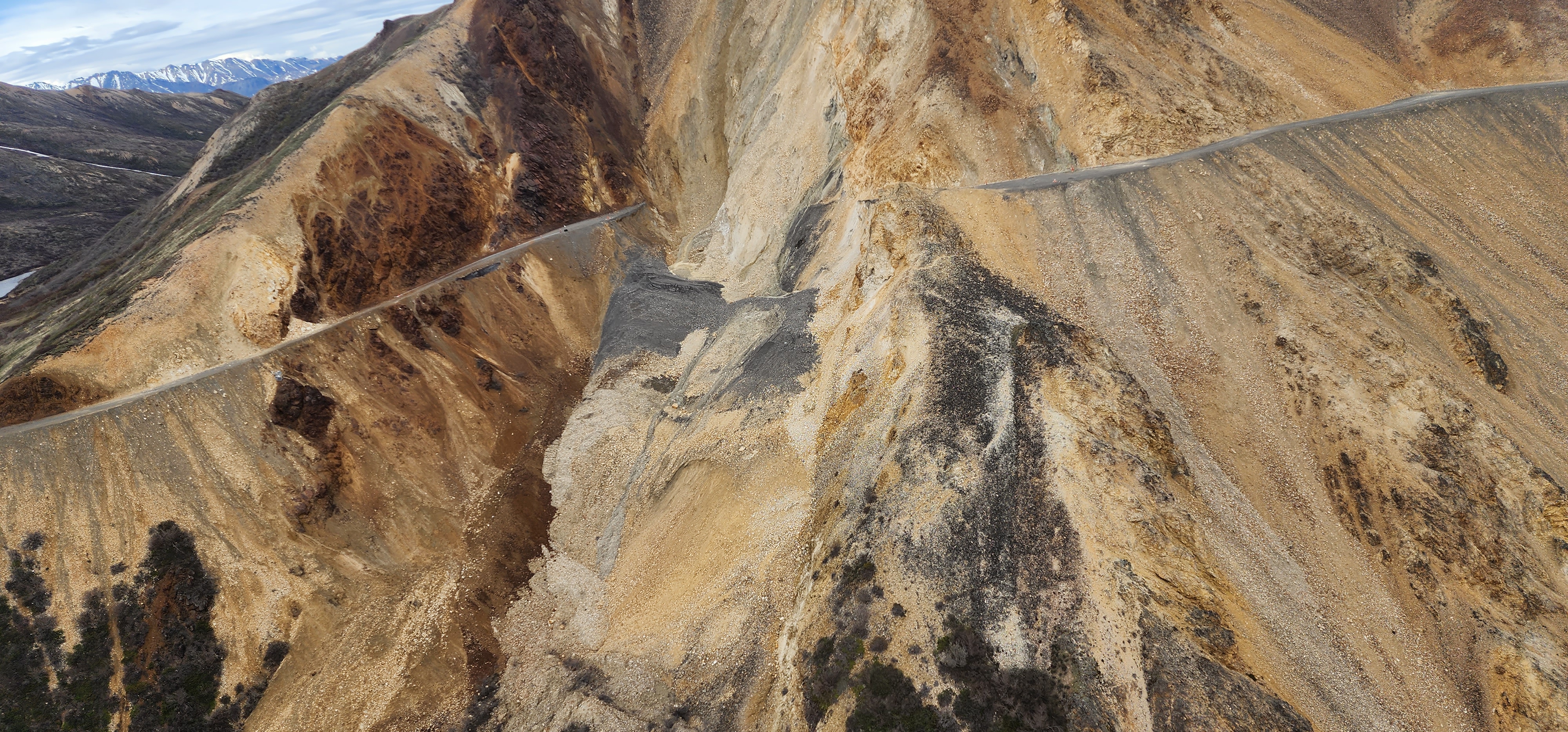20230606_173135 Aerial view of a steep rocky mountainside. A gray gravel road cuts horizontally across the orange rock of the slope. In the center, the road drops away abruptly and loose rock slumps down the slope.