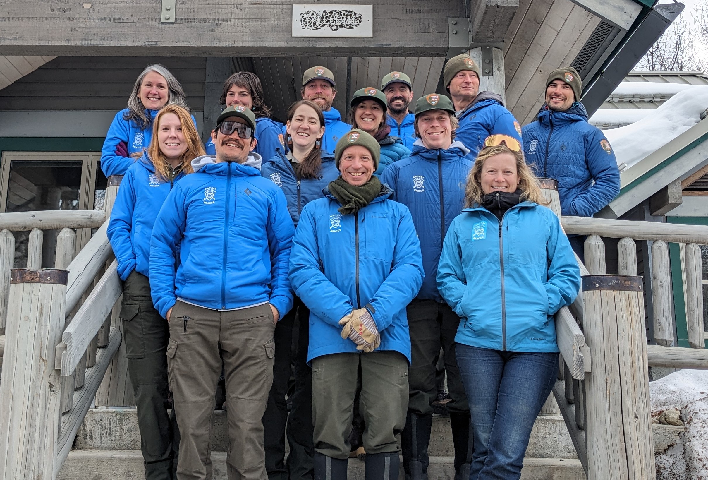 Walter Harper Talkeetna Ranger Station staff photo 2024 Photo of 13 rangers in blue jackets standing on the front steps of a ranger station