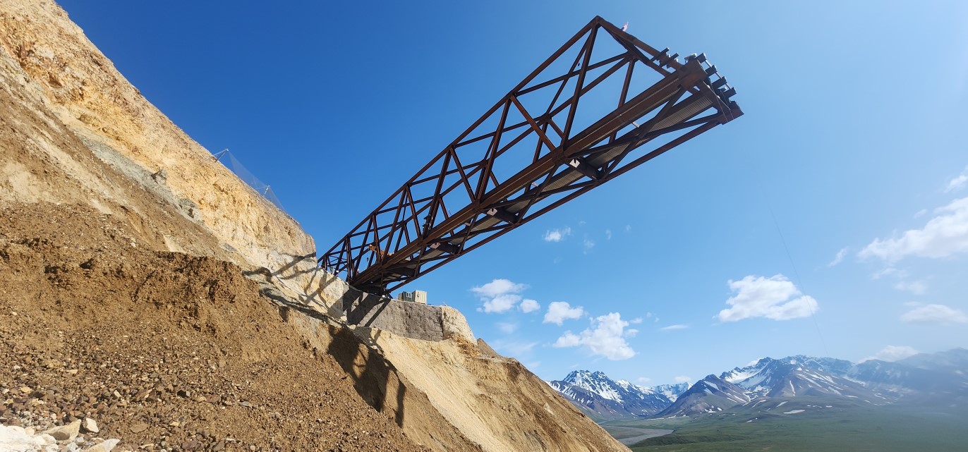 2025-06-26 bridge from in the slide proHNS Several trusses of the bridge extend out over the landslide above the viewer against a bright blue sky.