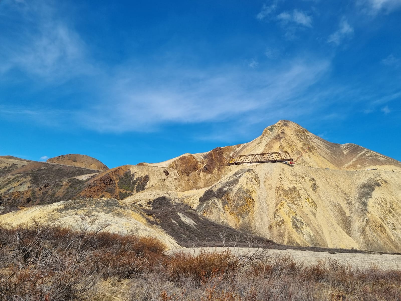 2025.06.02 courtesy of Rose Keller Looking up at the side of Polychrome mountain from a gravel river bar. Midway up the slope, several trusses of the bridge can be seen in progress on the east side of the landslide.