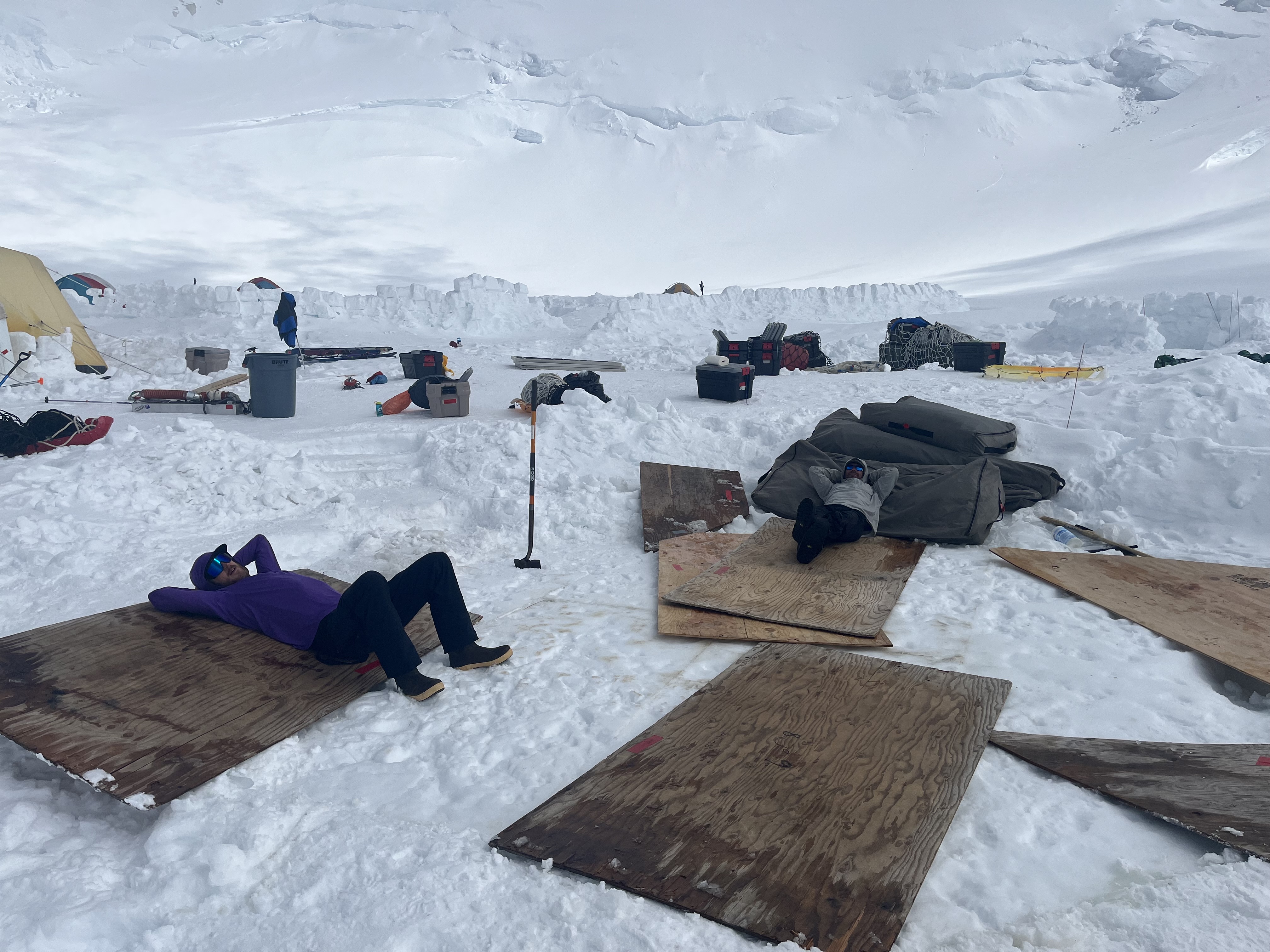 Brokedown Palace Two men rest on top of plywood sheets and large grey duffle bags