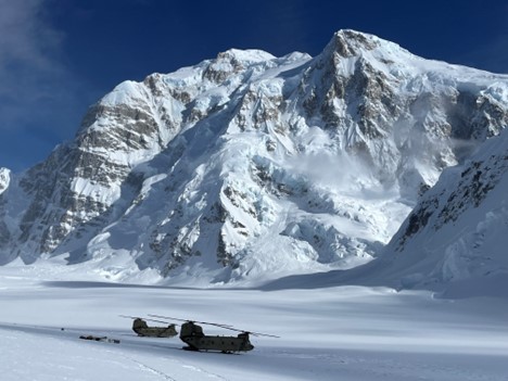 Two large helicopters at the base of a snow mountain