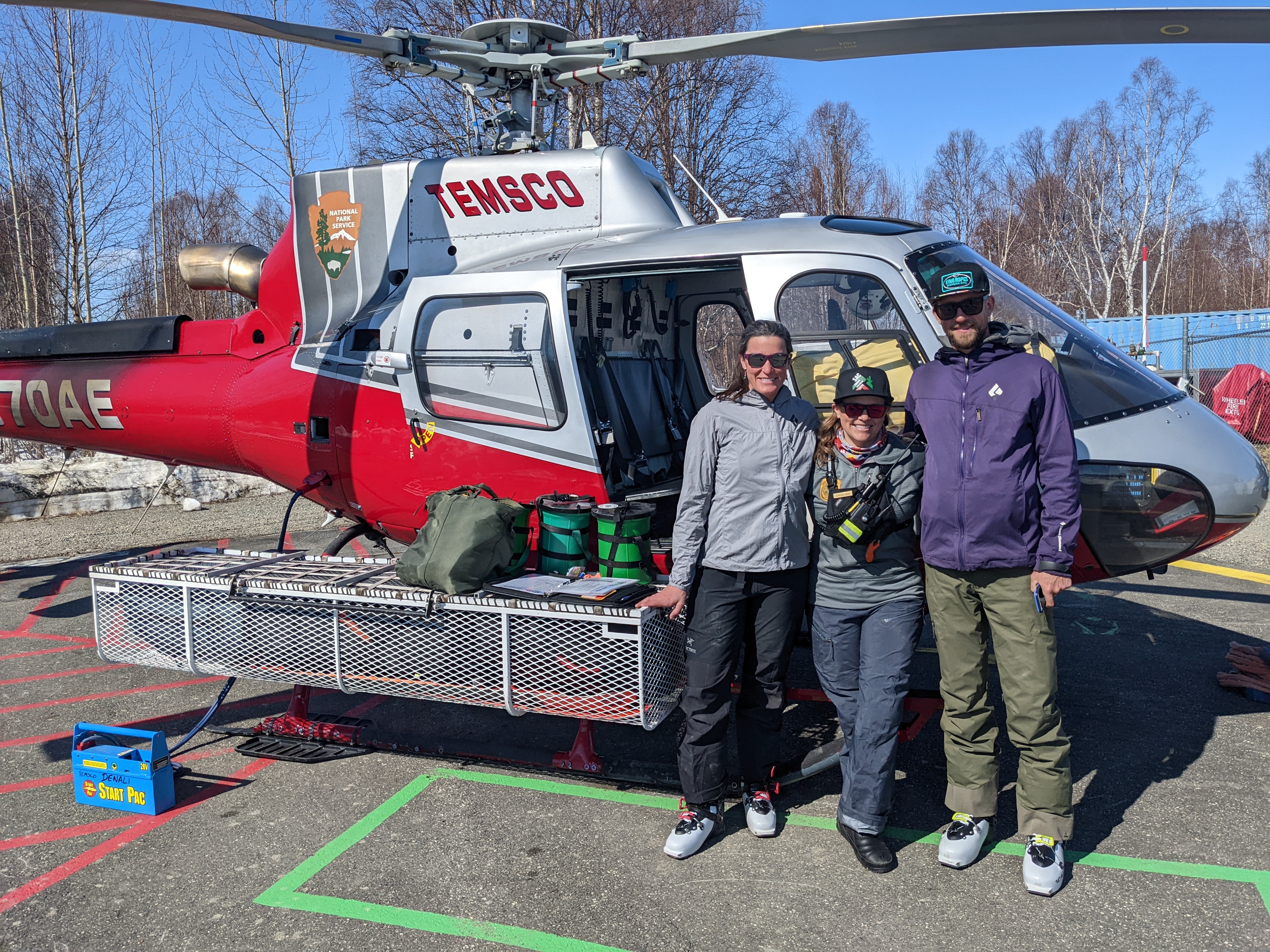 Three climbers stand outside the open door of a helicopter