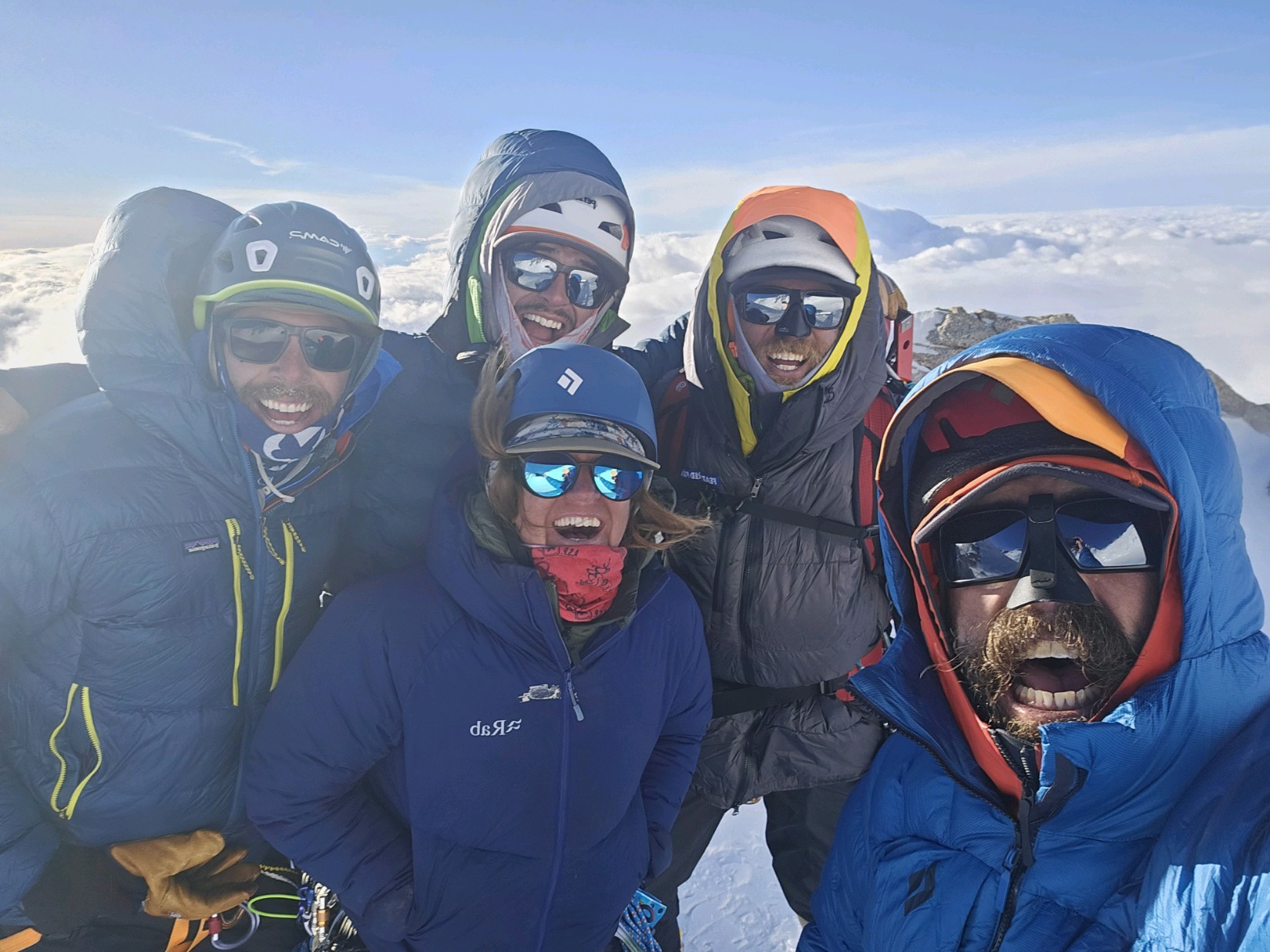 Closeup of five well-bundled climbers with clouds and mountain peaks in the backdrop