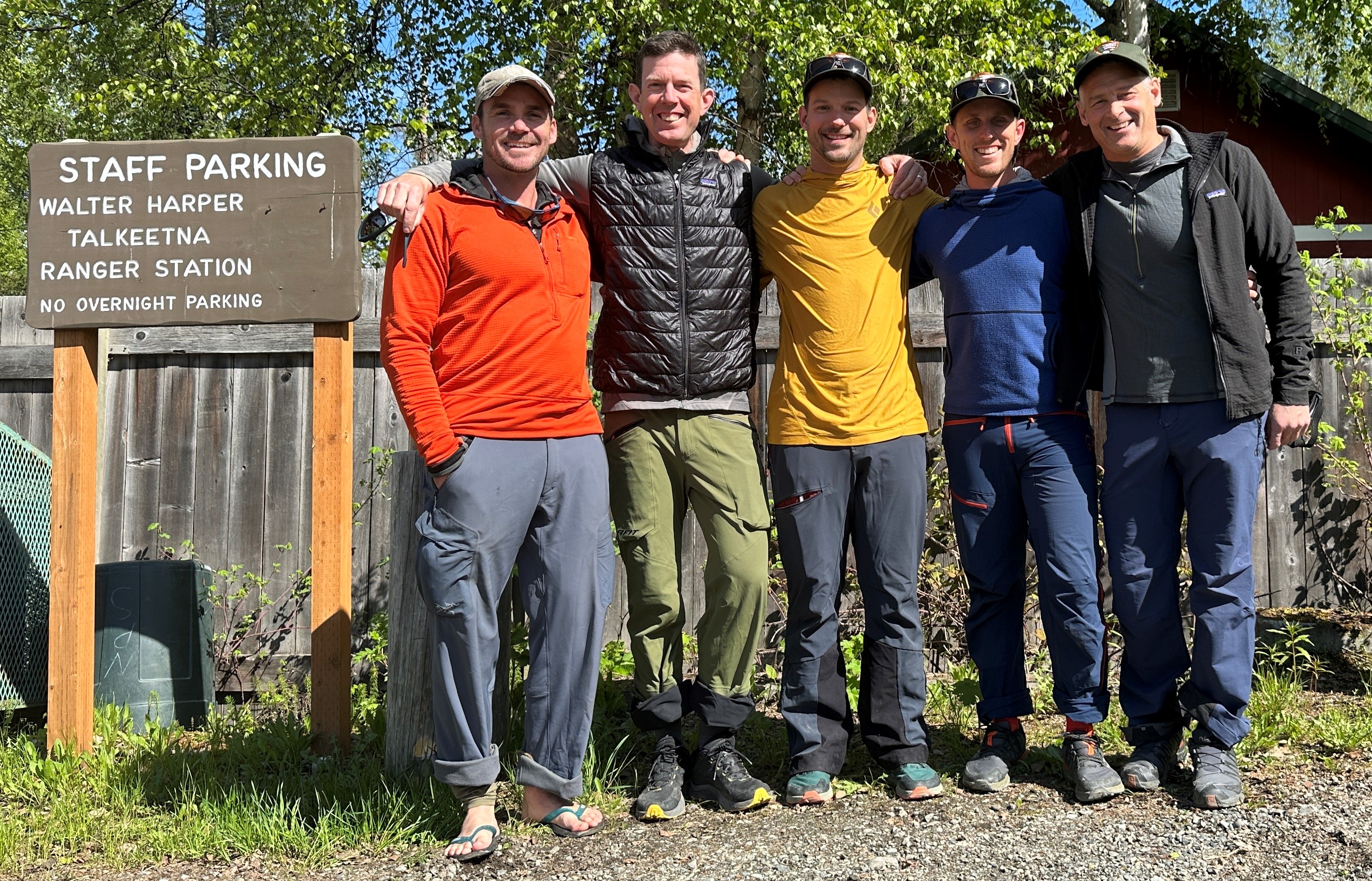 Five mountaineers stand next to a sign that says Walter Harper Talkeetna Ranger Station Staff Parking Only