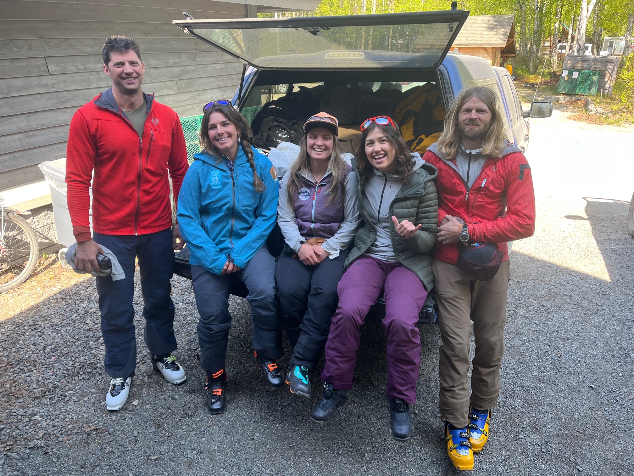 The Bombastic Patrol Five smiling climbers sit on the back of a pickup truck filled with duffel bags
