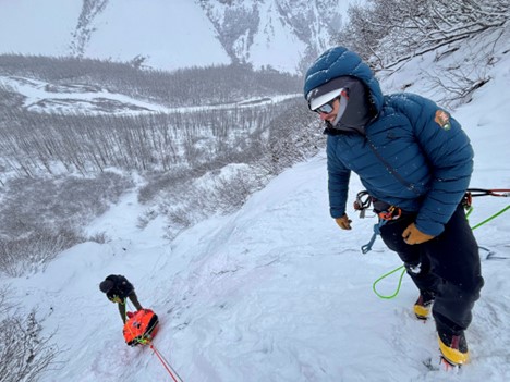 Two rangers on a snowy hillside pulling up orange rescue equipment