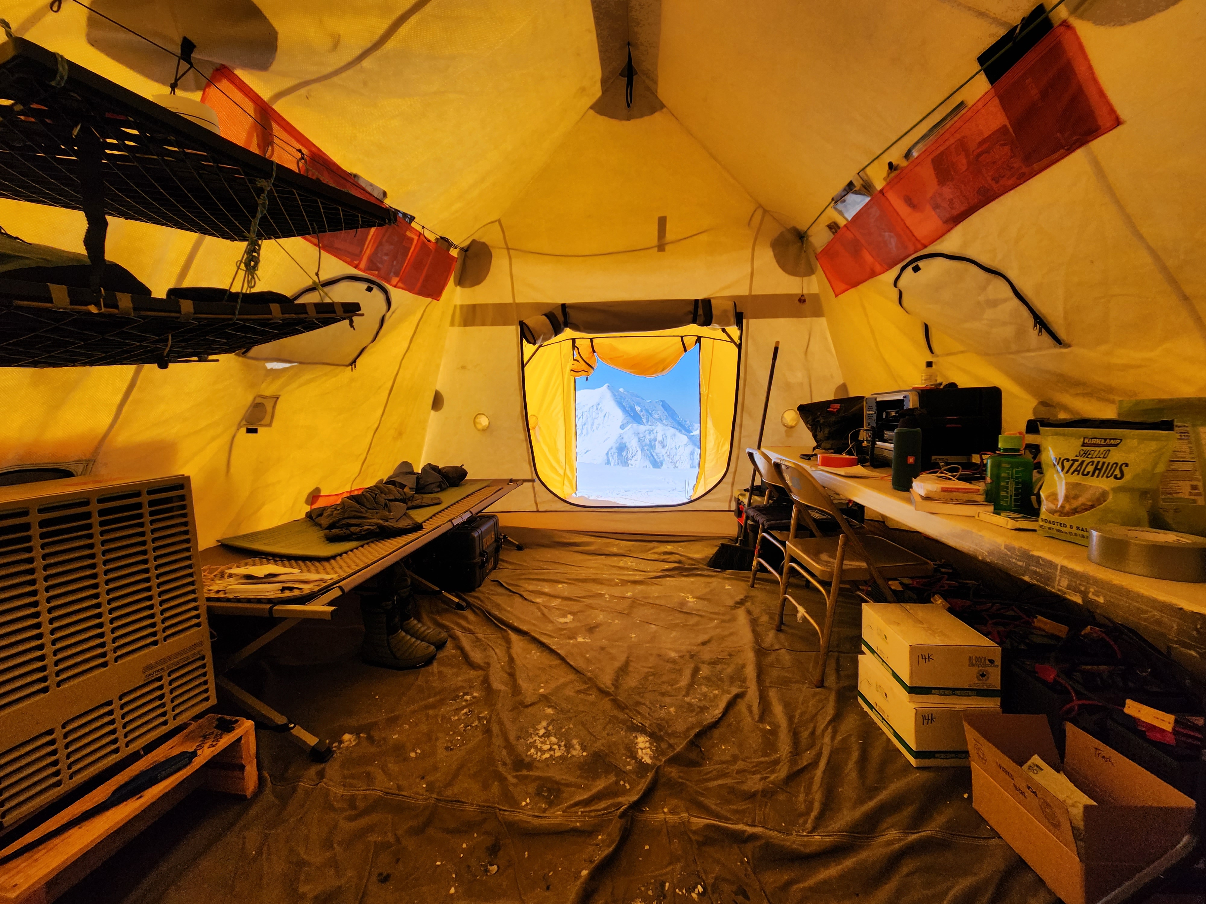 View of a tent fillied with a cot, a heater, batteries; the view out the tent door is of Mount Foraker